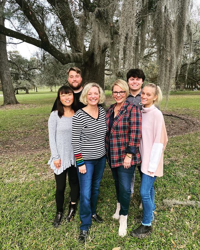 Kelli Carpenter in a black and white striped sweater and blue pants with her wife in red check shirt and navy jeans and children in different dresses.